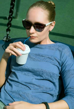 Girl in sunglasses drinking coffee from a paper cup on a sunny summer day