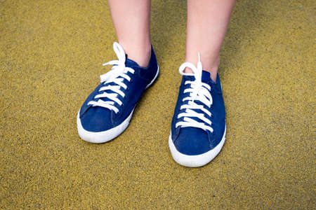 Female feet in blue sneakers on yellow coating on a day timeの写真素材