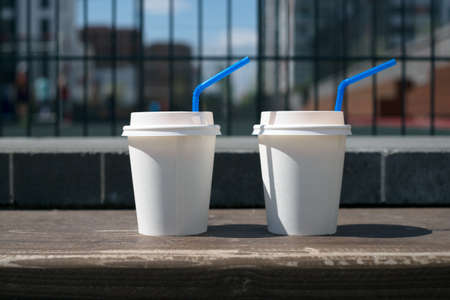 Two white coffee paper cups on the background of the fence from the gridの写真素材