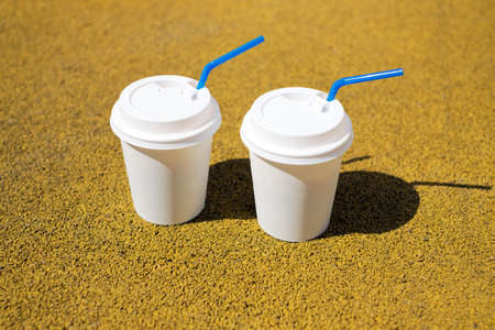 Two white coffee cup on a yellow paper coating on a sunny dayの写真素材