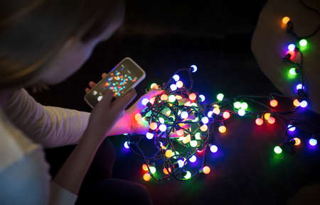 Hand girl photographed on a mobile phone colorful garlands of lightsの写真素材
