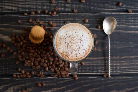 A cup of cappuccino coffee on a wooden background with a spoon and coffee grainsの写真素材