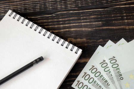 Euro banknotes notebook and pencil on  a dark wooden background