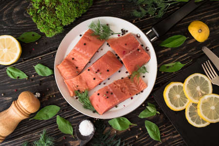 Salmon fillet on rustic kitchen table with fresh ingredients for tasty cooking and frying pan. Wooden background, frame, top view. Healthy and diet food concept.の写真素材
