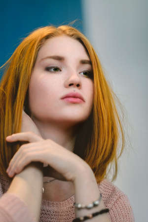Red-haired girl sits leaning back in his chair in a cafe. Redhead. Portrait of red-haired girl in a blouse closeup daytime.の写真素材