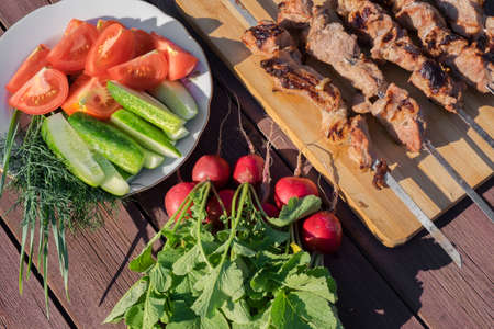 Grilled meat on skewers, radish and vegetables on a wooden background in red.の写真素材