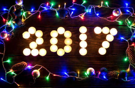 Happy new year 2017 written with burning candles. Christmas lights background. Holiday shiny garland border top view on brown wooden background. Winter holidays illumination. Happy New Year 2017.の写真素材