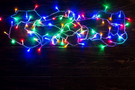 Christmas lights background. Holiday shiny garland border top view on brown wooden planks surface. Xmas tree decorations, winter holidays illumination. New Year.の写真素材