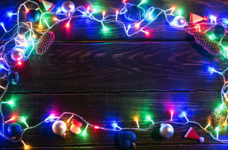 Christmas lights background. Holiday shiny garland border top view on brown wooden planks surface. Xmas tree decorations, winter holidays illumination. New Year.の写真素材