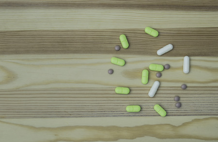 white capsules and green pills medication on a wooden tableの写真素材
