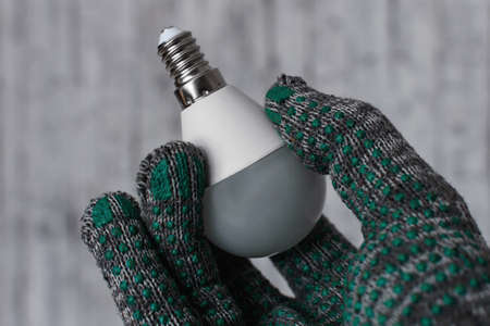 A man in gloves holds a new LED lamp in his hand.の写真素材