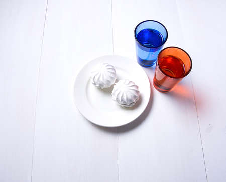 two colorful cups of water and a white plate on white wooden backgroundの写真素材