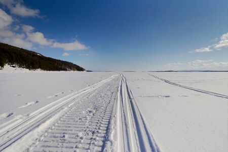 Snowmobile trail stretching into the distance against the blue sky and snowy expansesの写真素材