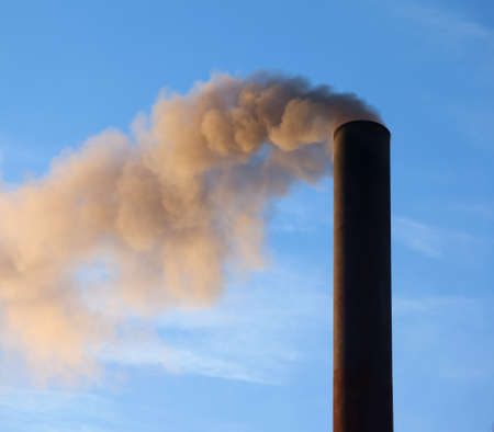 A large black smokestack sends smoke up into a clear blue sky.の写真素材
