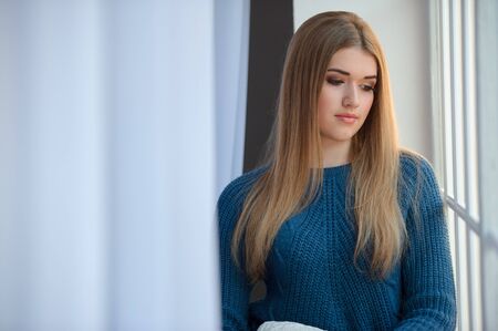 Girl in a blue woolen sweater waiting at the windowの写真素材