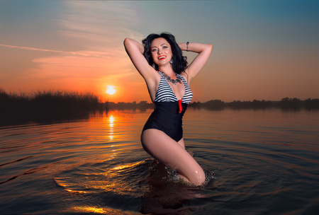 fashion photo of sexy hot beautiful girl model with dark hair in black and striped swimwear swimming in river or lake with red lips and fashion accessory and jewelryの写真素材