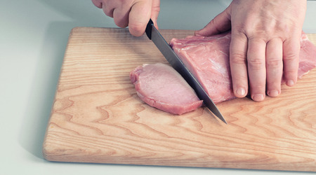 Closeup view man in the kitchen is cutting pork on cutting board Hands cutting meat