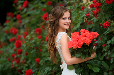 Young beautiful pretty girl with long hair and white dress standing and holding bucket red roses.の写真素材