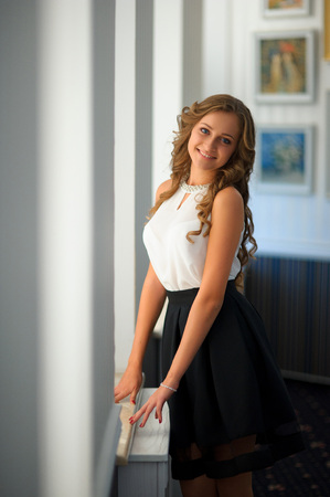 Portrait of a young beautiful caucasian woman with long brown hair against big white window indoors at homeの写真素材