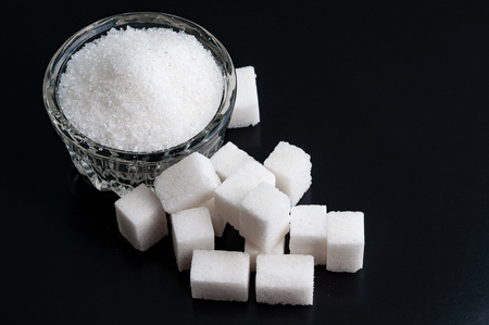 Top view on a Bowl with white granulated and refined sugar on black surface, close-up