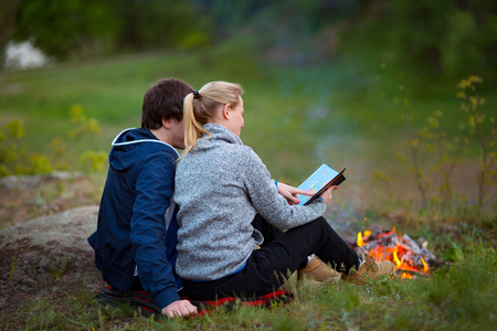 Couple hiking. Young couple sitting on grass near the fire embracing and examining the map. Travel, vacation, holidays and adventure concept. Forest Mountain landscape backgroundの写真素材