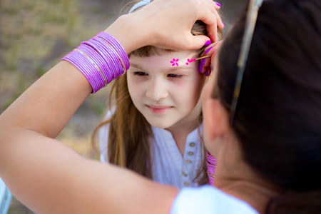 Cute little girl has her face painted with flowers before birthday partyの写真素材