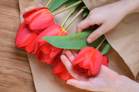 children's hands hold a bouquet of red tulips over a wooden table. Mother's Day concept.の写真素材