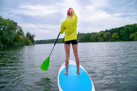 a woman stands on a SUP board on a large river on a cloudy day. Stand on the oars - great outdoor...