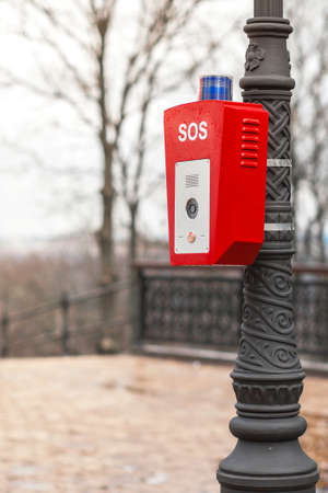 Help or police call button. SOS. A stand with a button is fixed on the street, on a lamppost. Red...