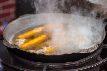 Street food. Boiling corn in a large cauldron, and thick boiling water rises above boiling water. On the street in the city.の写真素材