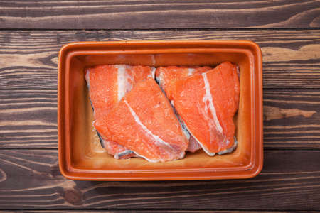 Pickled steaks of red fish. In a ceramic bowl on wooden boards. Shot from above.の写真素材