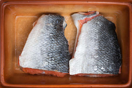 Pickled steaks of red fish. In a ceramic bowl on wooden boards. Shot from above.