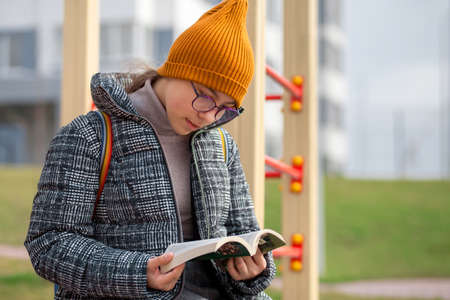 Clever teen girl is reading a book in the playground. Children reading, learning in the parkの写真素材