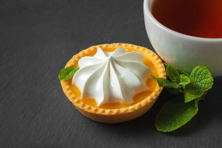 Lemon tart with mint leaves and a cup of tea. Confectionery background on a black slate plateの写真素材