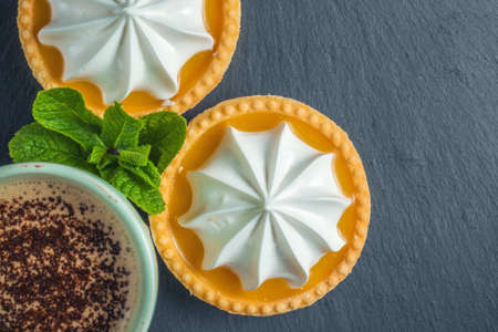 Lemon tart with mint leaves and a cup of cappuccino with chocolate topping
