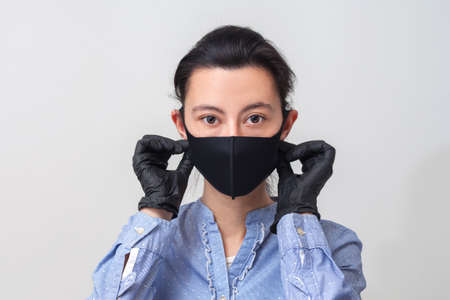 The girl in gloves puts on a medical mask. Light gray-blue background. In a respiratory mask.の写真素材