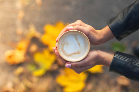 A cup of coffee in the hands of a girl. Top view, only female palms with the sleeves of a black...