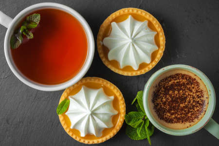 Lemon tart with mint leaves, a cup of tea and a cup of cappuccino with chocolate toppingの写真素材