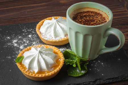 Lemon tart with mint leaves and a cup of cappuccino with chocolate toppingの写真素材