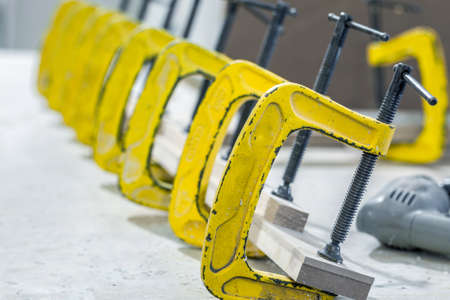 Manufacturing of wooden furniture in a factory. Gluing furniture parts with clamps. Selective focus.の写真素材