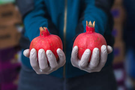 Fresh pomegranates in gloved hands at the vegetable market. Healthy food concept. High quality photoの写真素材