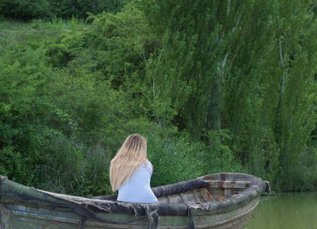 thoughtful girl in an old boat, seen from behindの写真素材