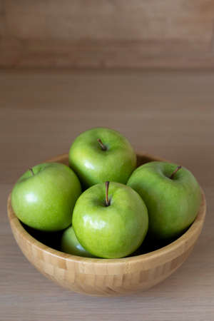 Green apples in a wooden bowl on the table.の写真素材