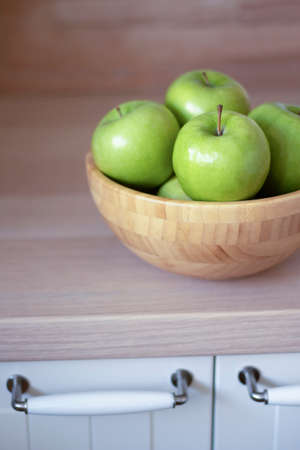 Green apples in a wooden bowl on the kitchen table. See the handles of the kitchen table doors.の写真素材