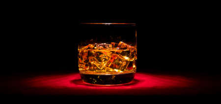 A glass of whiskey on the rocks on the red table in the middleの写真素材
