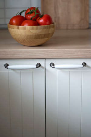 Wooden bowl with red tomatoes on a branch on the kitchen table with a large view of the kitchen table doorsの写真素材