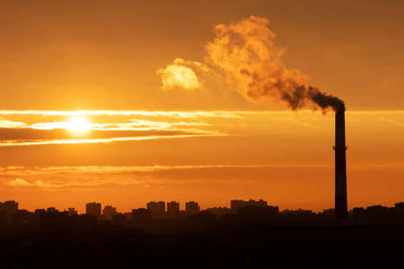 Sunrise over the silhouette of houses on the outskirts of the metropolis landscape with a Smoking pipe in Russiaの写真素材