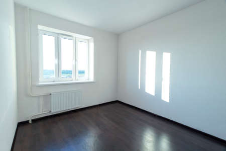 An empty clean room with white walls, a white radiator and dark laminate flooring. A closed window. The light on the wall is in the form of a window.の写真素材