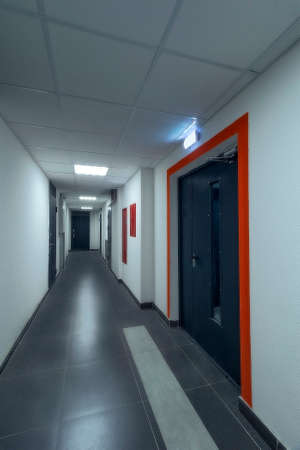 An empty, clean corridor of an apartment building, with white walls and gray tiles on the floor. A...