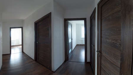 Panoramic photo of the apartment corridor with white walls, dark wooden doors and dark laminate flooring.の写真素材